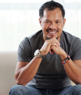 Handsome Filipino man sitting on sofa and smiling at camera